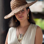 Woman wearing a white lace vest, straw hat, and earrings with a blurred background